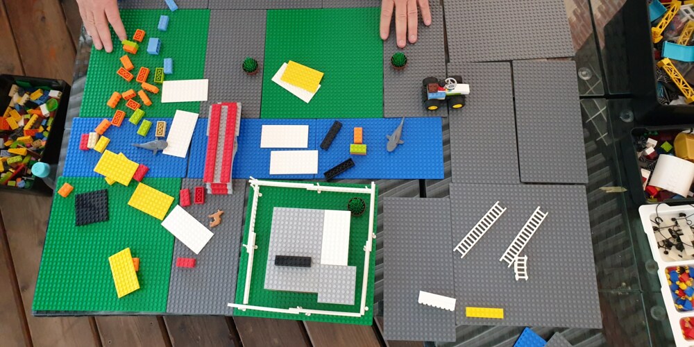 Grüne, blaue und graue Legoplatten markieren den Grundriss der Lego-Stadt. Darauf liegen noch viele verschiedene Steine chaotisch herum.