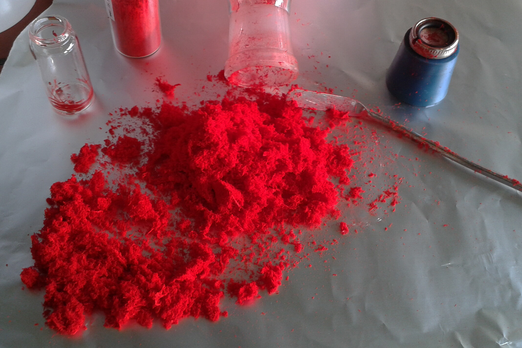 Ein knallrotes, fluffiges Puder liegt auf einer Alufolie. Ein Metallspatel liegt daneben.
